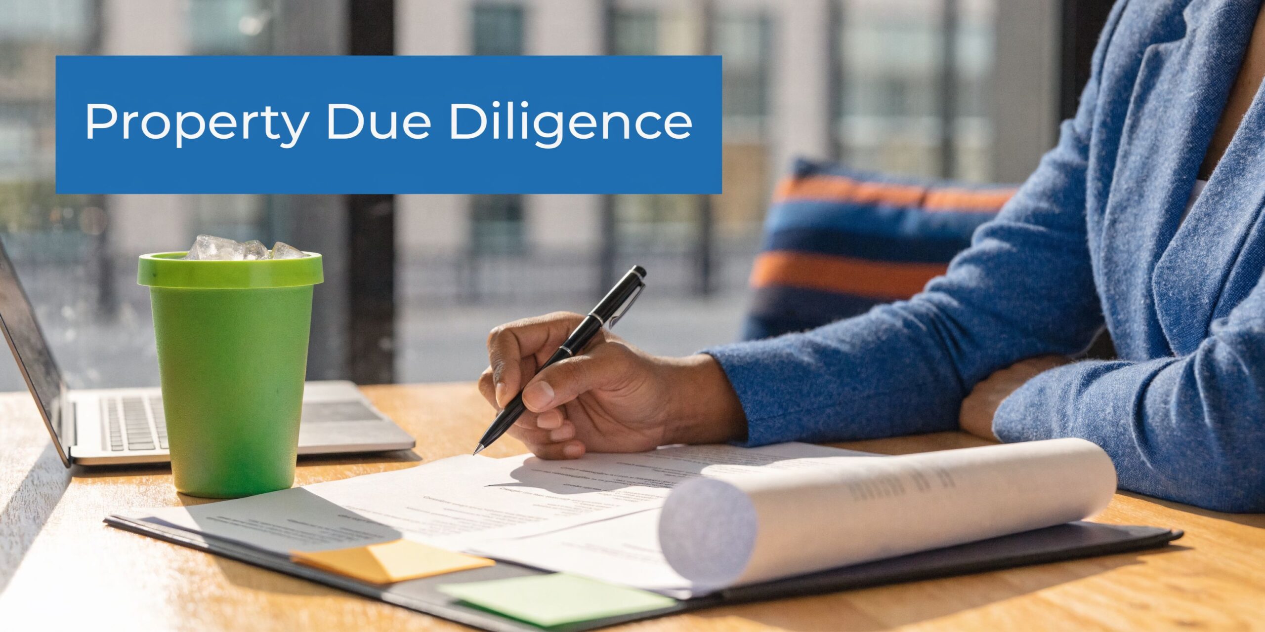 A professional in a blue blazer reviewing property due diligence documents while working at a desk.