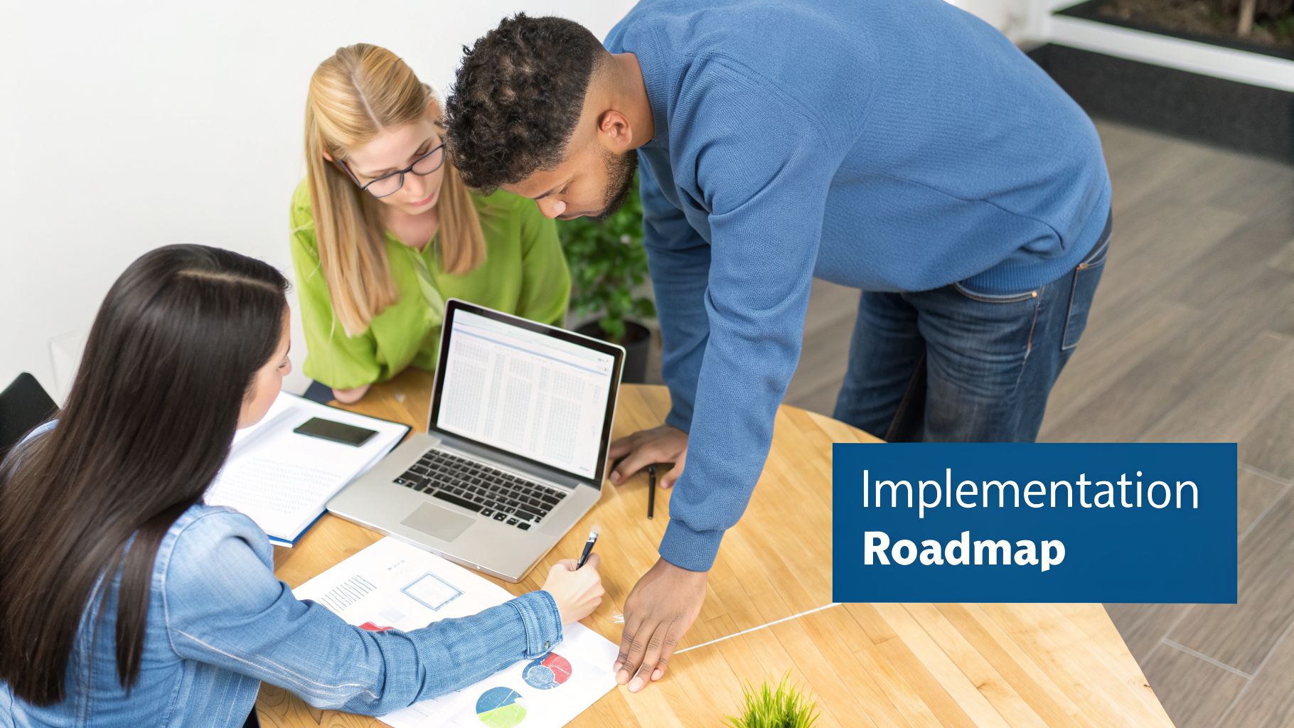 Diverse team collaborates on an implementation roadmap, reviewing data on a laptop and documents on a wooden table.